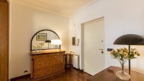 Un couloir avec une commode en bois, un miroir, une lampe et une porte.