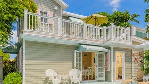 Una casa de dos pisos con balcón, piscina y mobiliario de exterior.