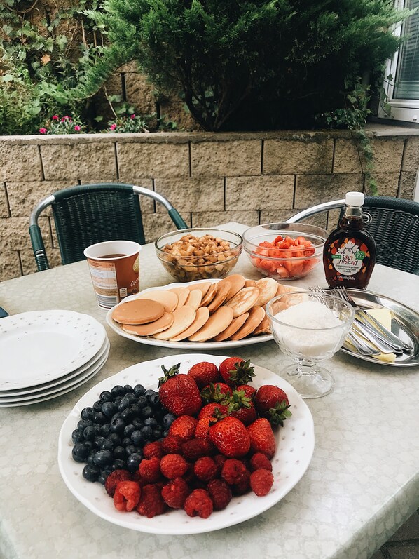 A table set outdoors with plates of pancakes, berries, and a bottle of syrup.