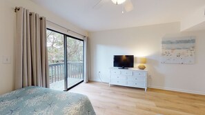 A bedroom with a bed, a TV on a white dresser, a balcony with curtains, and a painting on the wall.