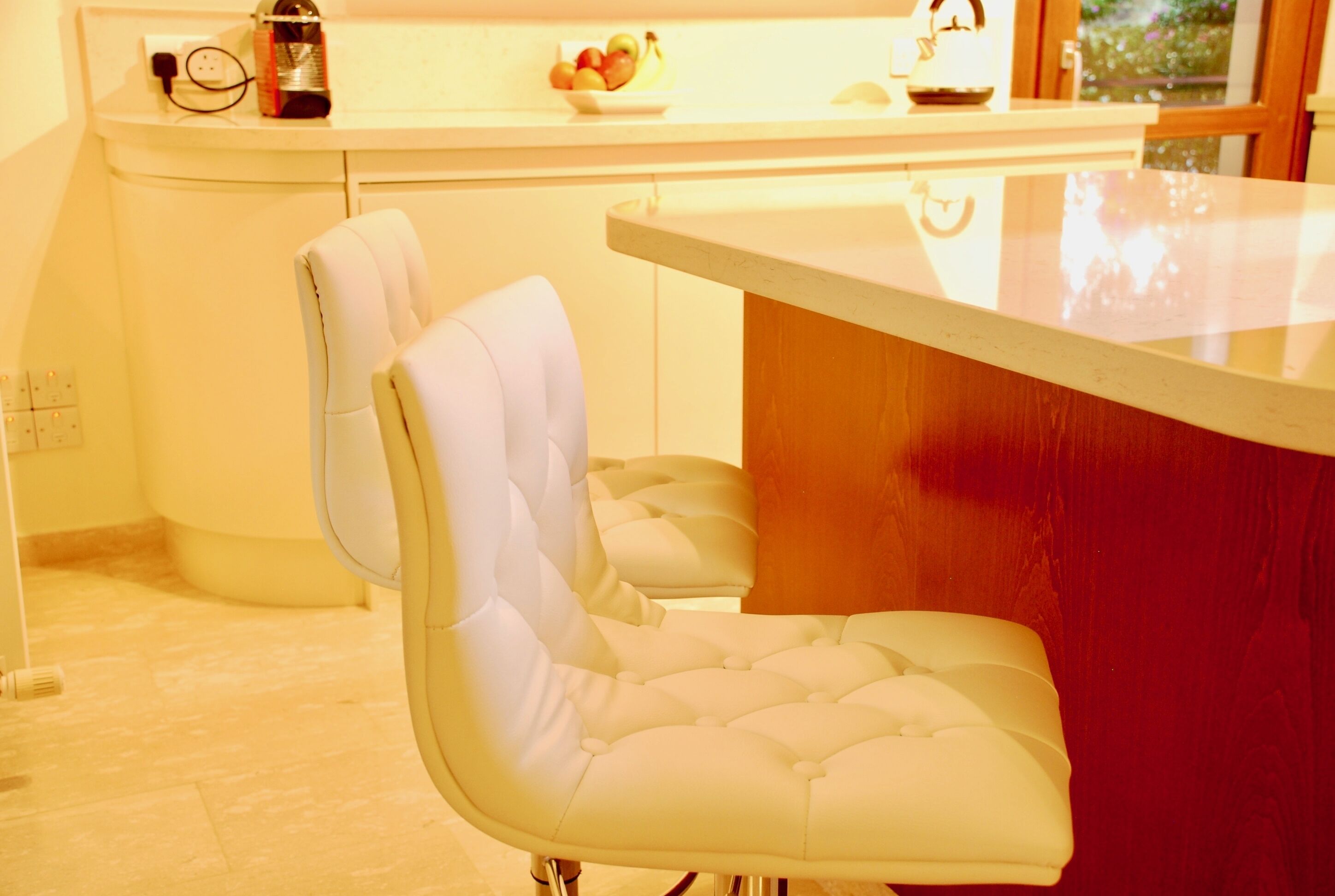 Une cuisine moderne avec un plan de travail blanc, un mur d’accent rouge et une chaise recouverte de tissu blanc.