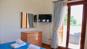 Habitación de hotel con cama, cómoda de madera, televisor montado en la pared y puerta corrediza de vidrio al exterior.