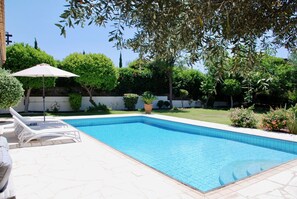A rectangular swimming pool with tiled edges, surrounded by a tiled patio. There are lounge chairs and a single umbrella on the patio. - 3 bedroom Villa Pera 12 with 10x5m private pool, within walking distance to resort village square, resort facilities, Aphrodite Hills (Kouklia)