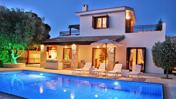 Una casa moderna de dos pisos con piscina, mobiliario exterior y un patio bien iluminado.