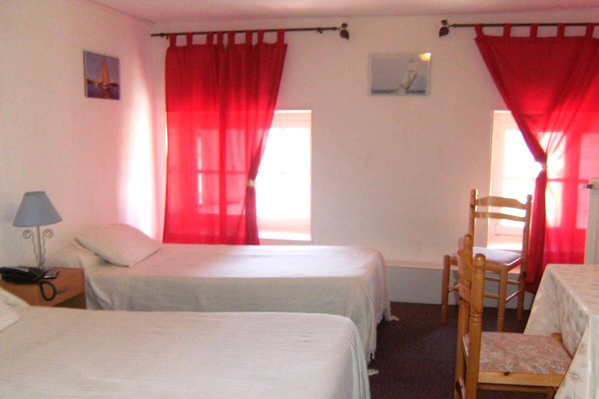 A room with two single beds, a wooden chair, a small table, and a lamp.