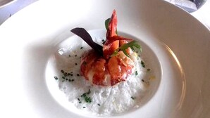 A white plate with a seafood dish, possibly shrimp, garnished with herbs and a decorative element. - Hotel le Vendangerot (Rully)