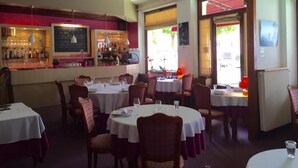 A restaurant interior with round tables, chairs, a bar area, and a chalkboard menu. - Hotel le Vendangerot (Rully)
