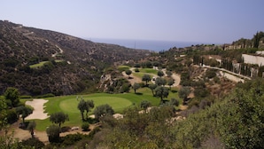 Um campo de golfe com uma vista panorâmica do mar e colinas.