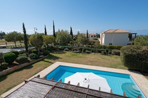 A swimming pool with a white umbrella, surrounded by a well-maintained garden and a house in the background.