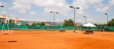 A tennis court with a net, green banners, and a bench.
