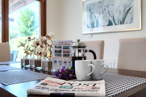 A table with a newspaper, a coffee pot, two white cups, and a floral arrangement.