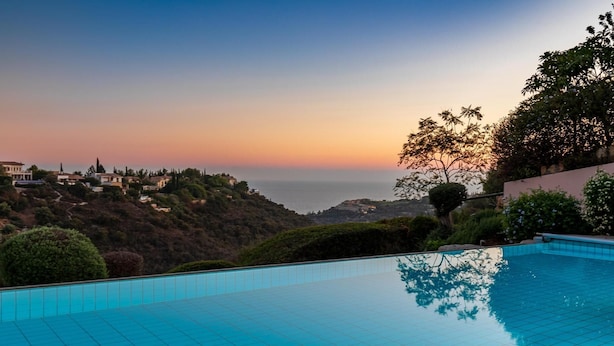 Ein Schwimmbecken mit Blick auf eine Küstenlandschaft im Sonnenuntergang.