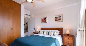 A bedroom with a bed, two bedside tables with lamps, a wooden wardrobe, a ceiling fan, and two framed pictures on the wall. - Villa 98 Helidonis - Four Bedroom Villa, Sleeps 8 (Kouklia)
