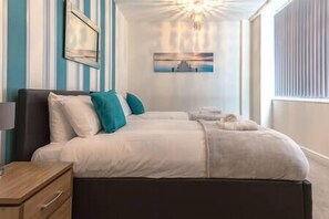 A bedroom with a bed, bedside tables, a nightstand, and a painting on the wall. - Comfortable Swindon 2 bedroom Town Centre Apartment with en-suite, FREE Parking (Swindon)