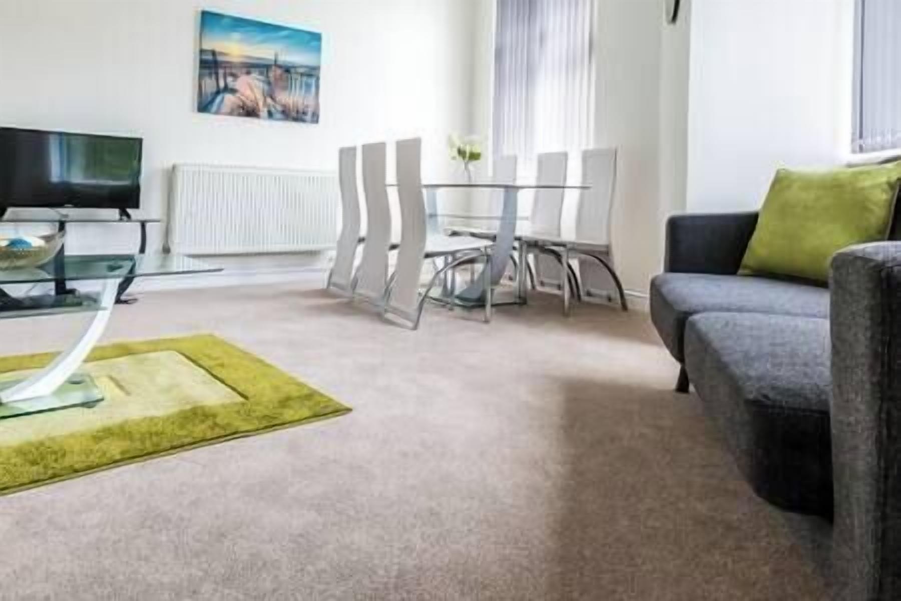 A modern living room with a glass coffee table, a grey sofa, and a dining table with chairs.