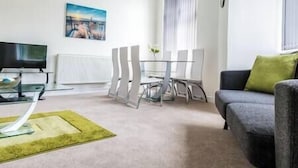 Un salon moderne avec une table basse en verre, un canapé gris et une table à manger avec des chaises.