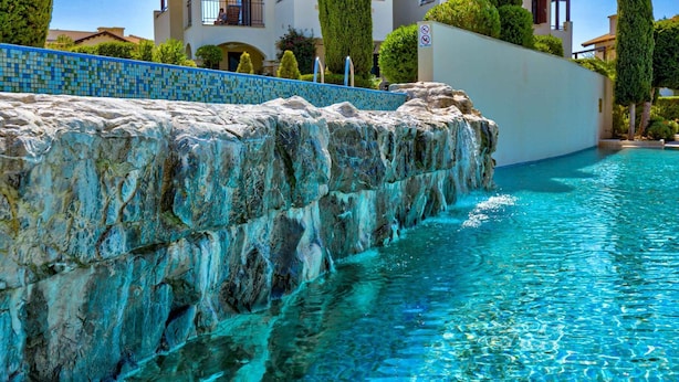A swimming pool with clear blue water, a stone wall, and a tiled border. - Apartment DC01 - Kalypso (Kouklia)