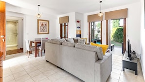 A modern living room with a grey sofa, wooden dining table, and a TV on a stand. - Apartment DC01 - Kalypso (Kouklia)