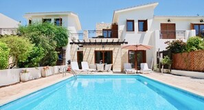 Ein Poolbereich mit Liegestühlen und einem Tisch, umgeben von einem weißen Gebäude mit Steinverzierungen und einem Balkon.