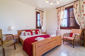 Une chambre à coucher avec un lit en bois, une chaise, une table de chevet, une lampe et une fenêtre avec des rideaux.