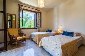 Une chambre avec deux lits, une chaise, une fenêtre avec des rideaux et une table de chevet avec une lampe.