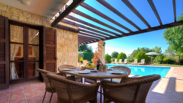 En uteplats med en pool, flätade stolar och en mur av sten.