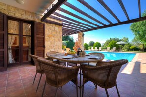 An outdoor patio with a pool, wicker chairs, and a stone wall. - 3 bedroom Villa Anarita 64 with private L-shaped pool, beautiful gardens, near resort village square (Kouklia)