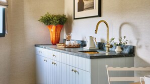 A kitchen with a sink, a coffee maker, a vase with flowers, and a framed picture on the wall.