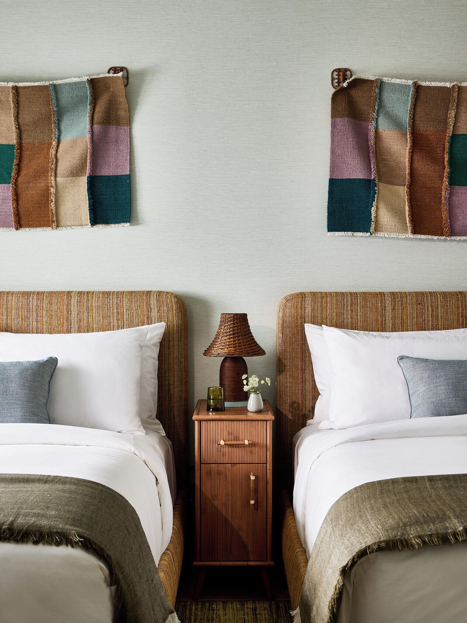 Une chambre d’hôtel avec deux lits, une table de chevet avec une lampe et une courtepointe accrochée au mur.