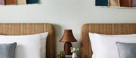Habitación de hotel con dos camas, una mesita de noche con lámpara y un colcha colgada en la pared.