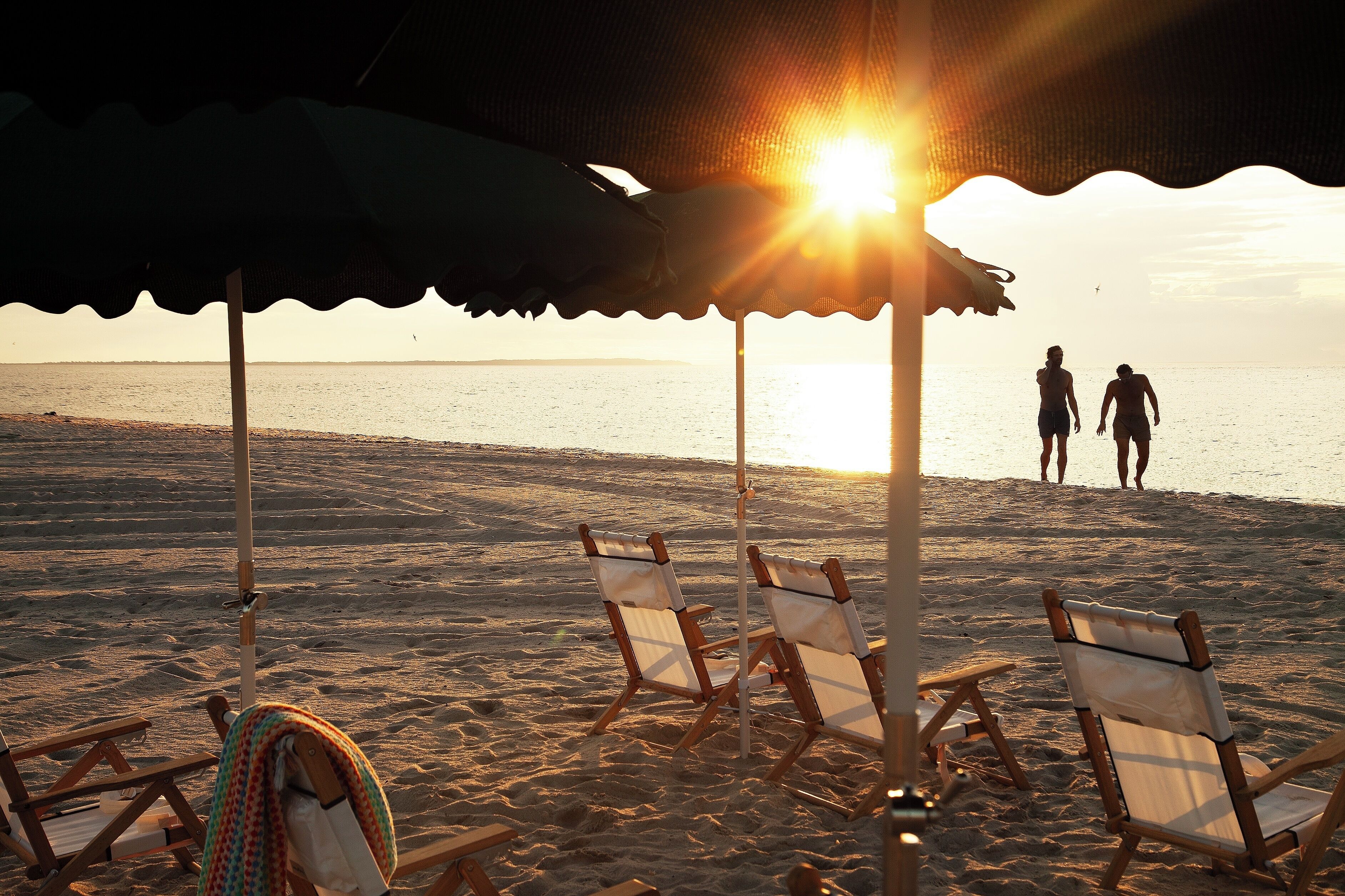 Une scène de plage avec des parasols et des chaises de plage, un ciel dégagé et l’océan en arrière-plan.