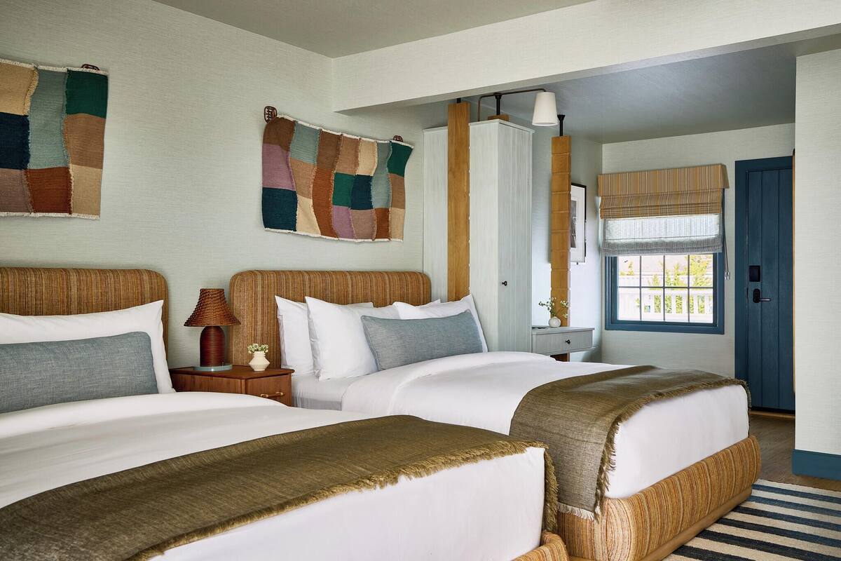 Hotelkamer met twee bedden, een groot raam met uitzicht, een deur en een muur met wandkleed.