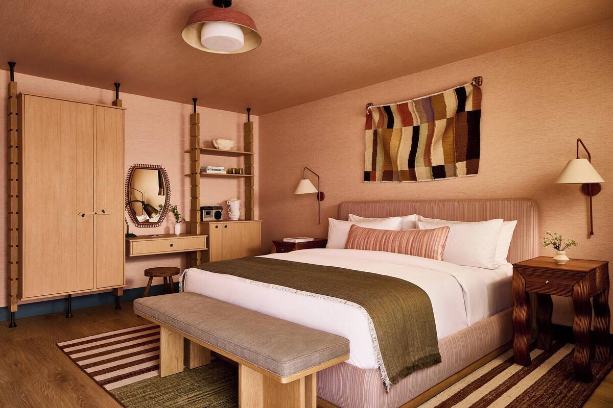 Een slaapkamer met een bed, nachtkastjes, een bankje, een kledingkast en een wandlamp.