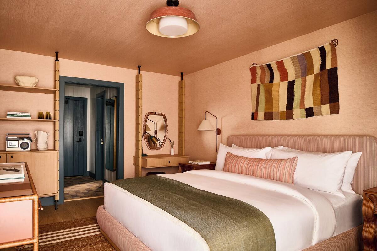 Een hotelkamer met een bed, een bureau, een stoel, een dressoir, een spiegel, een lamp en een wanddeken.