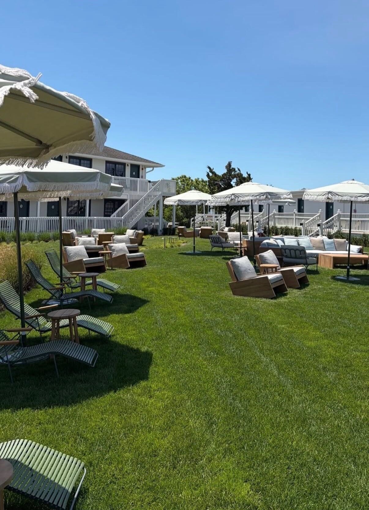 A well-maintained outdoor lounge area with multiple seating options including lounge chairs and tables, surrounded by white umbrellas providing shade.