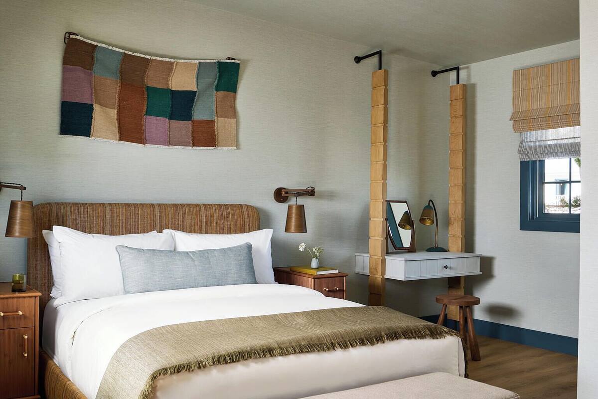 Een netjes ingerichte slaapkamer met een bed, nachtkastjes, een bankje, een hanglamp, een spiegel en een raam met gordijnen.