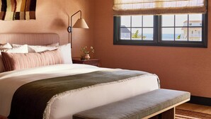 A bedroom with a bed, bedside lamp, window with view, and a hanging tapestry.