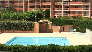 A hotel with a swimming pool, surrounded by greenery and a multi-story building with balconies. - APPARTEMENT LES RIVES DE LA FAVIERE (BORMES-LES-MIMOSAS)