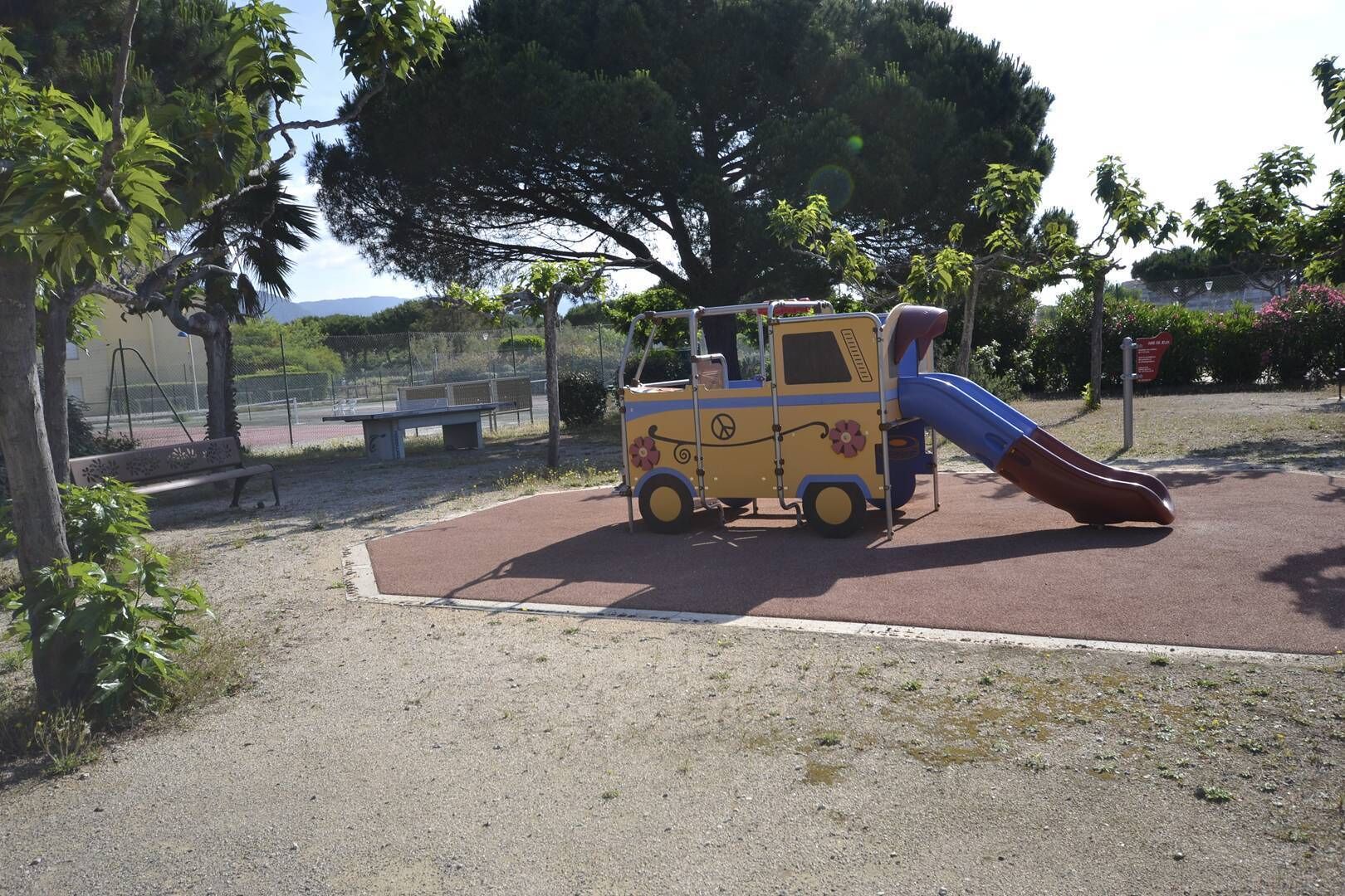 Un'area giochi con una struttura ricreativa a tema veicoli, inclusa una scivolo, in un parco con panchine e alberi.