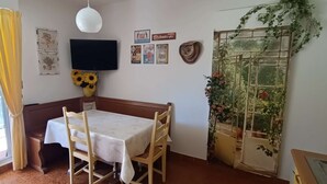 A room with a table and chairs, a TV mounted on the wall, and a window with curtains. - STUDIO L'AMIRAUTE (BORMES-LES-MIMOSAS)