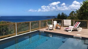 An infinity pool with a wooden deck, lounge chairs, and a view of the ocean. - In Guadeloupe in Bouillante Bungalow, the White Wolf of the Perched Cabins (Bouillante)