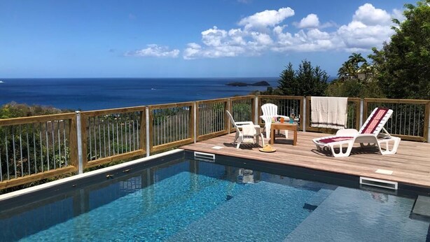 Una piscina infinita con terraza de madera, sillones de descanso y vista al océano.