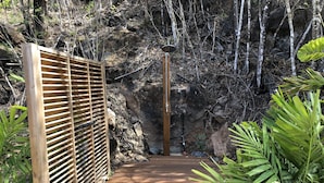 Una terraza de madera que conduce a una zona rocosa con una reja metálica y un caño.