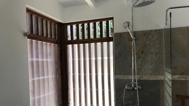 A bathroom with a shower, a window with blinds, and a view of greenery outside. - In Guadeloupe in Bouillante Bungalow, the White Wolf of the Perched Cabins (Bouillante)