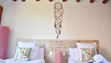 A room with two beds, each with a floral pillow, a wooden headboard, and a small round table with a pink lamp.