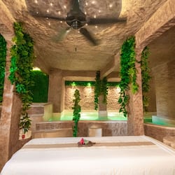 Relax in a serene space with a large bed, unique rock-like ceiling, and lush green walls, featuring a soothing water feature in the background.