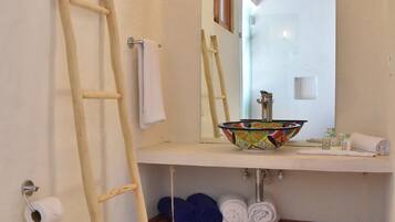 Un baño con una escalera de madera, un inodoro blanco, un lavamanos con un cuenco de colores y un espejo.