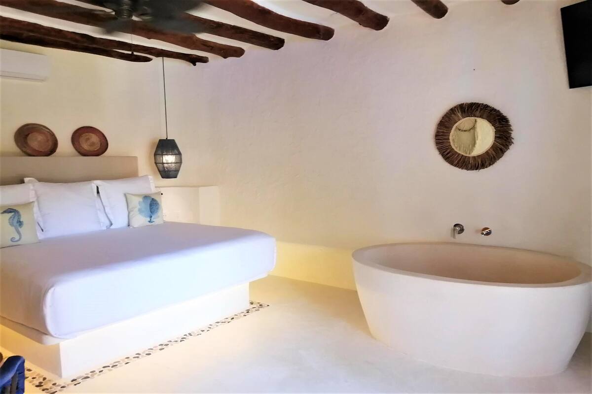 A bedroom with a large bed, a bathtub, and a wall-mounted mirror.