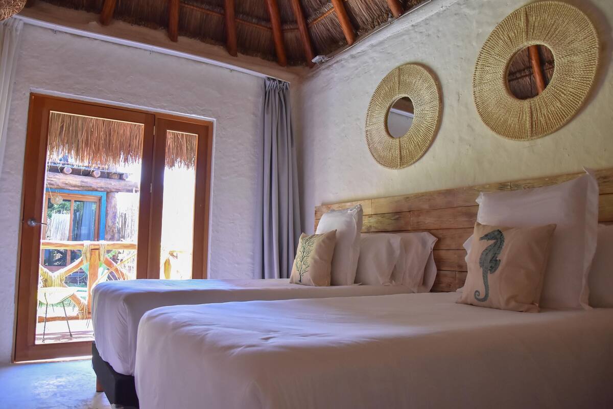A bedroom with a bed, pillows, and a wooden headboard. There are two circular wall decorations and a door leading to an outdoor area.