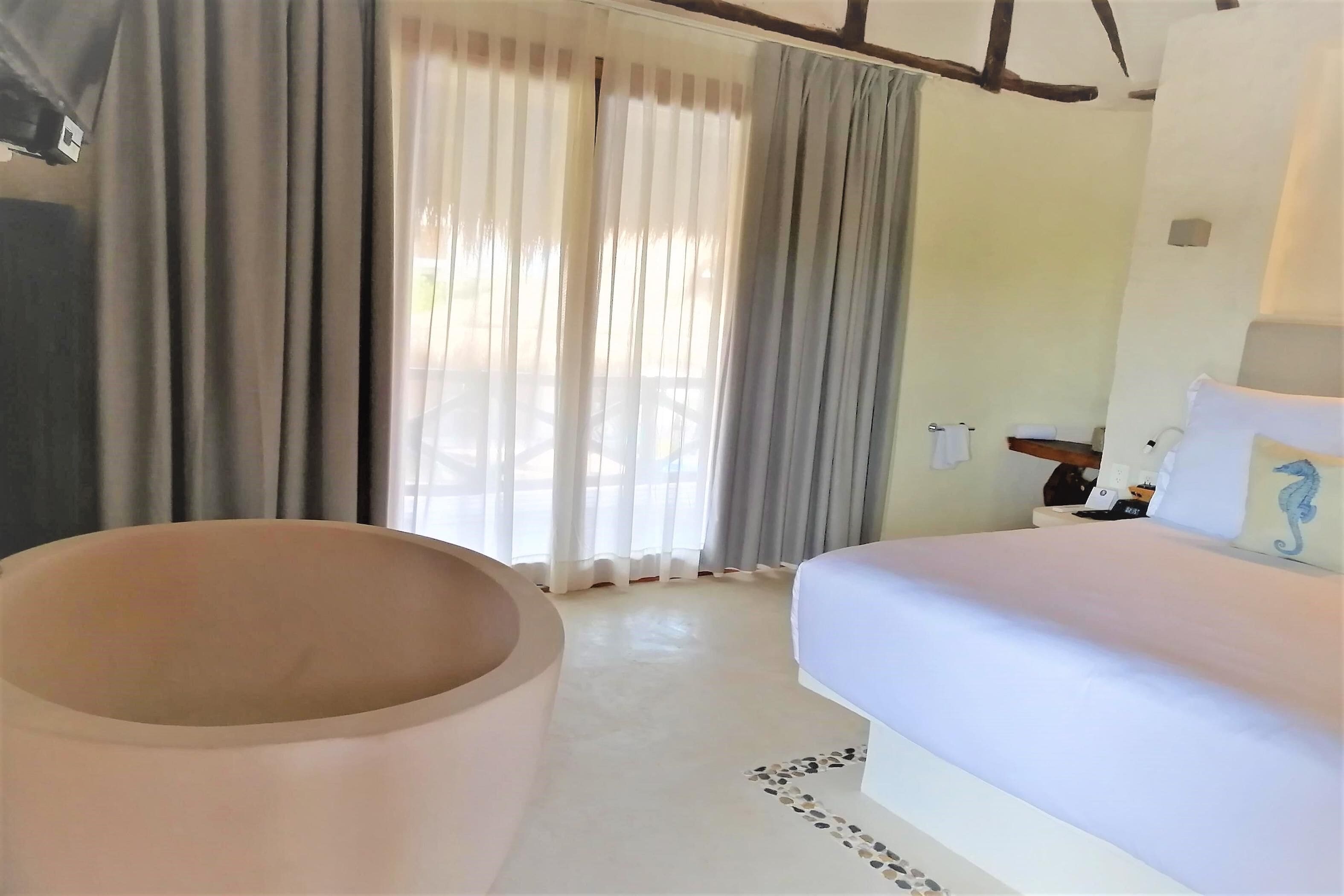 Een slaapkamer met een bed, een zitgedeelte met ronde stoelen en een raam met gordijnen.